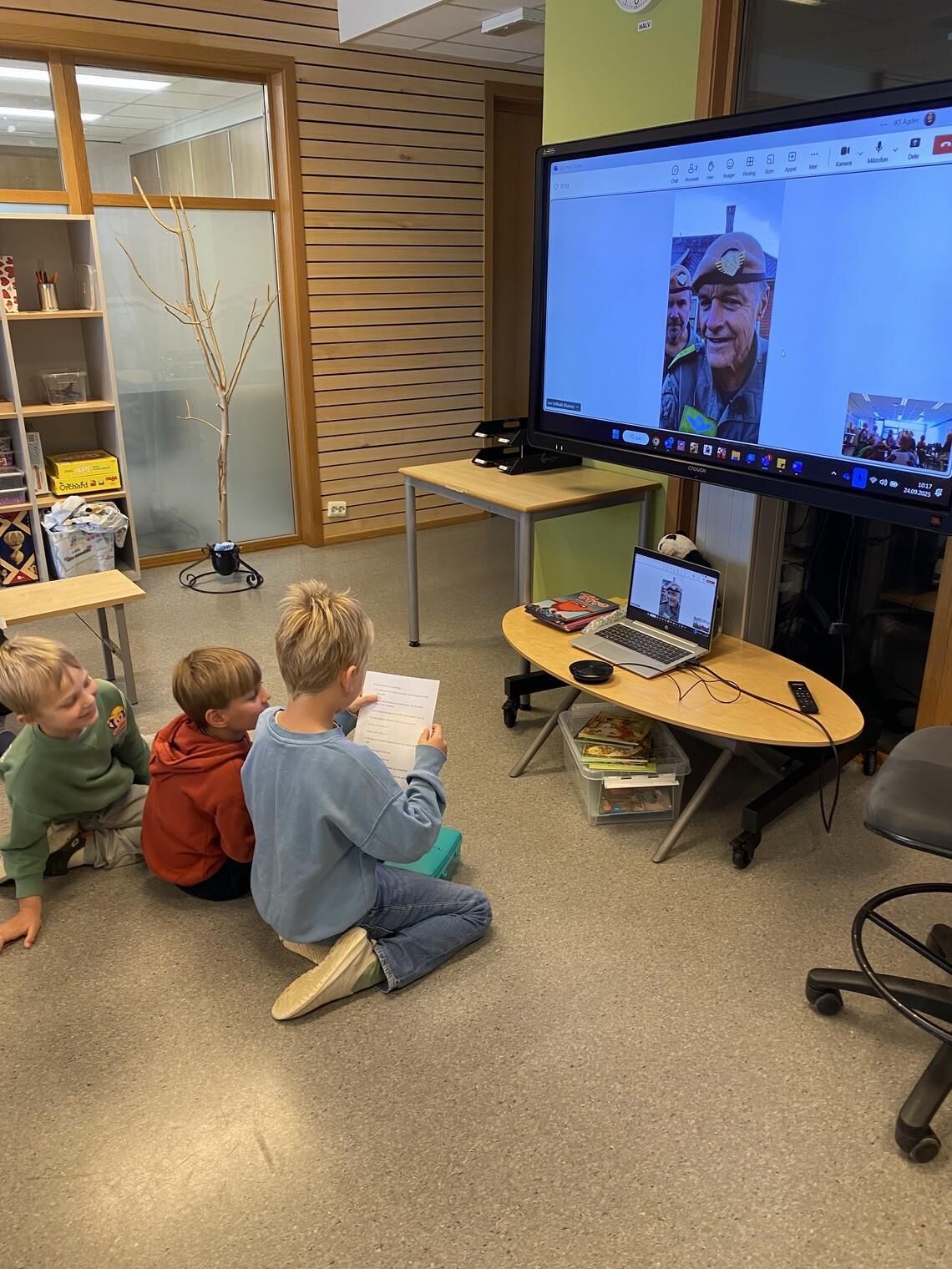 Barn sitter foran en skjerm hvor to menn snakker - Klikk for stort bilde