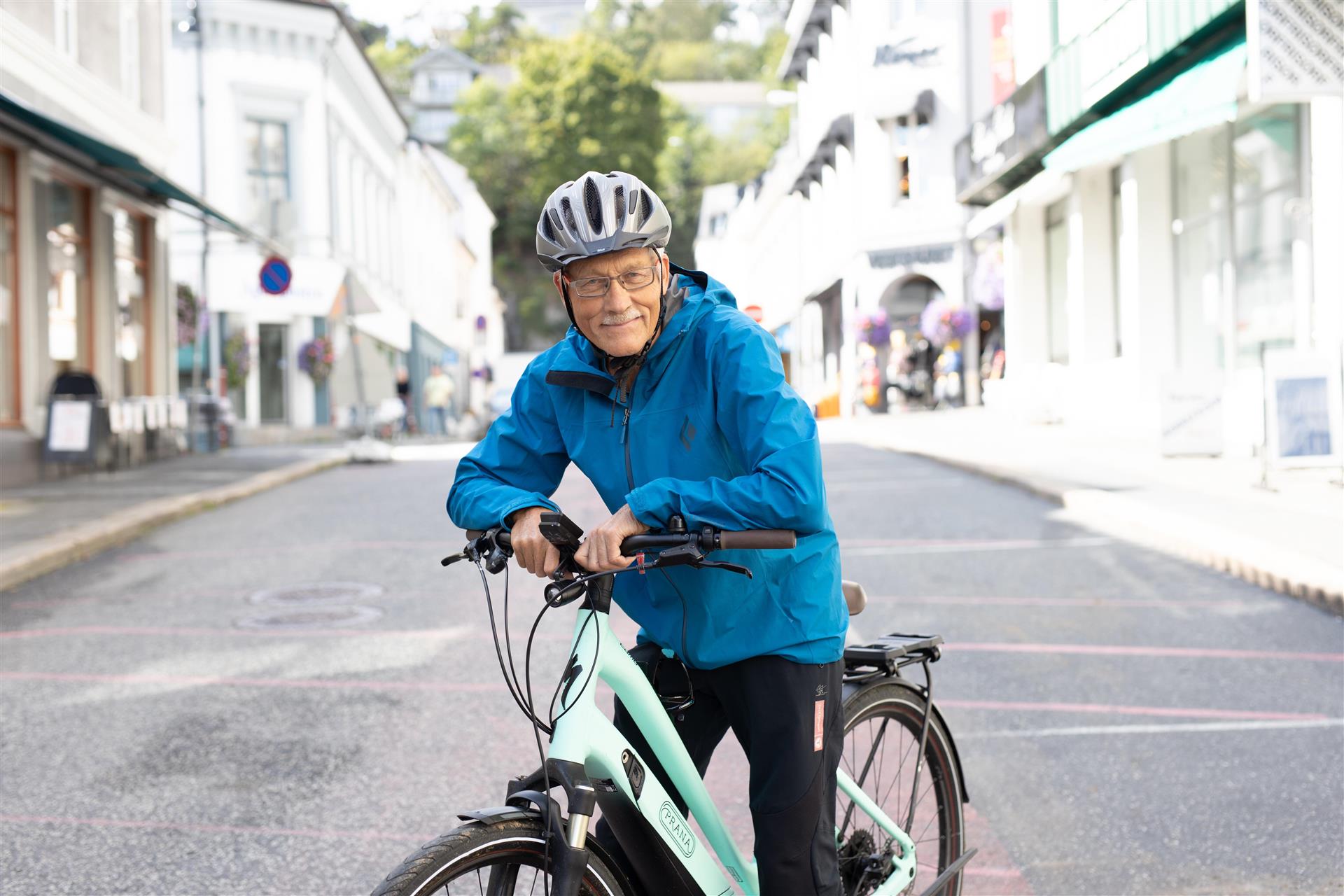 En eldre mann smiler og lener seg på en elsykkel