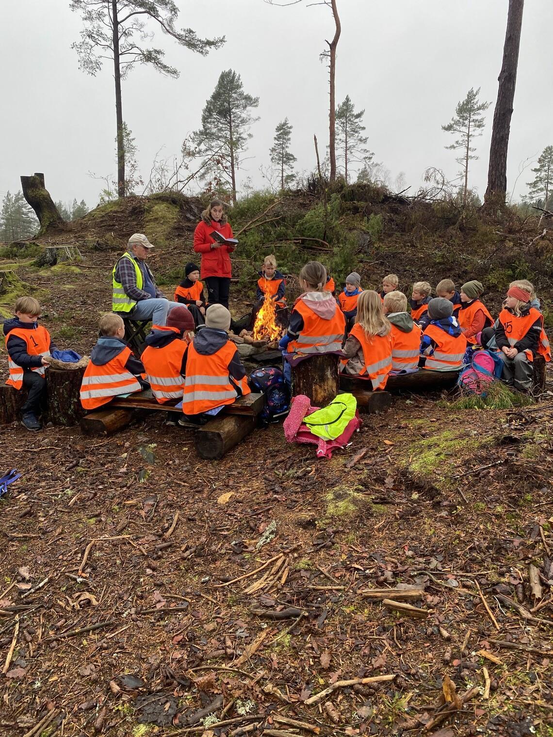Barn med refleksvester sitter rundt et bål - Klikk for stort bilde