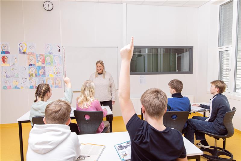 Elever sitter i et klasserom foran læreren. To elever rekker opp hånden.